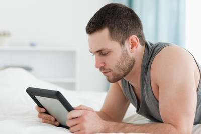 man using tablet while lying on bed