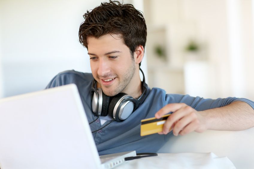 A guy wearing headphones and holding a credit card while looking at his computer