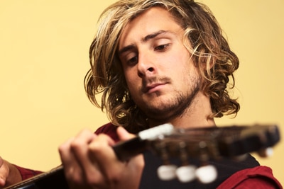 Young handsome Caucasian man playing the guitar (Selective Focus, Focus on the left eye)