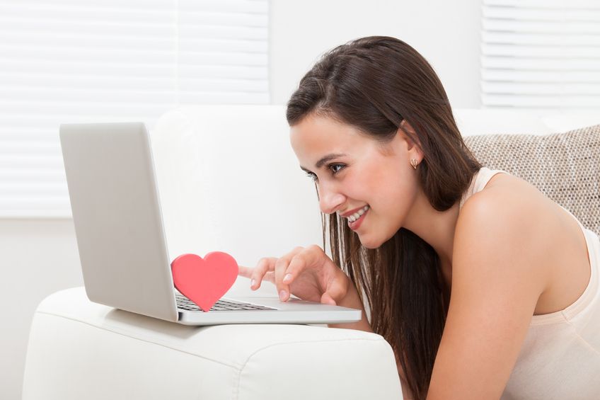 woman on a couch looking at her laptop and smiling