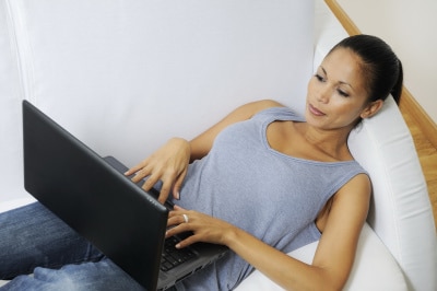 woman lying on bed while responding emails using her laptop