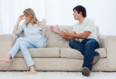 A man sitting on a couch is having an argument with his girlfriend who has her head turned away