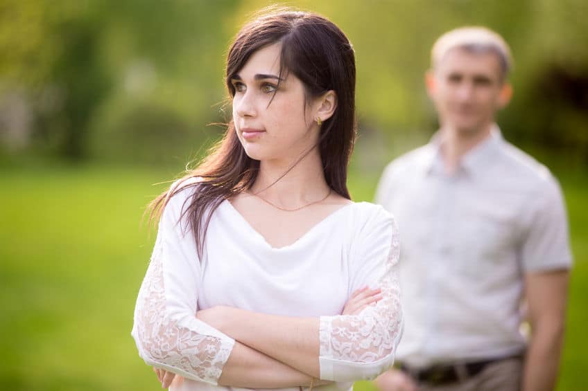 woman cross-armed, her man in the background