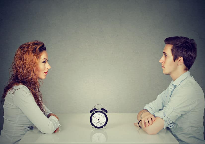 man and woman facing at each other, alarm clock in the middle