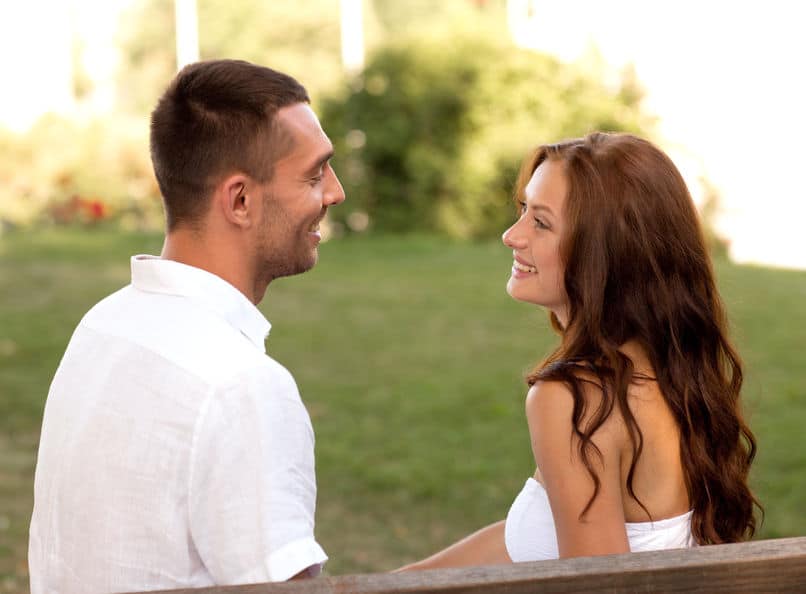 young couple smiling, looking at each other, sitting on a bench