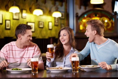 woman in between two men, having dinner while drinking beer