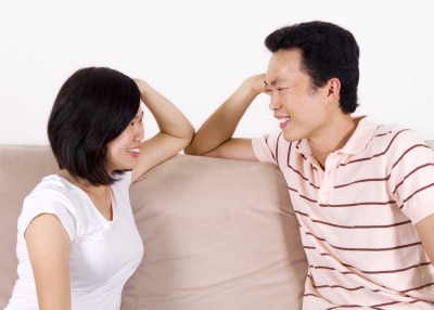 young Asian couple sitting on the sofa, smiling at each other