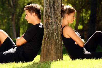 young couple separately sitting under a tree, being in conflict