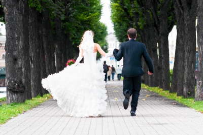 bride and groom running with joined hands on city park road