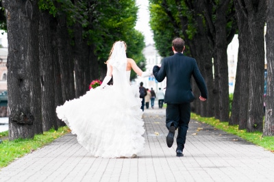 bride and groom running with joined hands on city park road