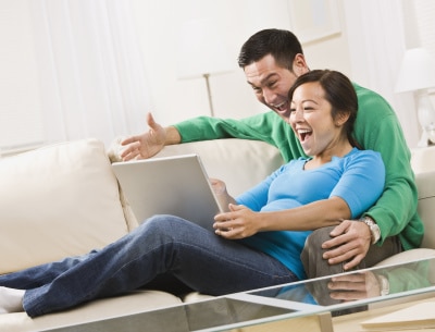 young couple sitting on the couch watching on their laptop, laughing