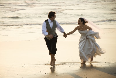 groom and bride running barefoot on beach