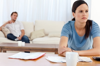 Angry woman doing her account while boyfriend relaxed on the sofa