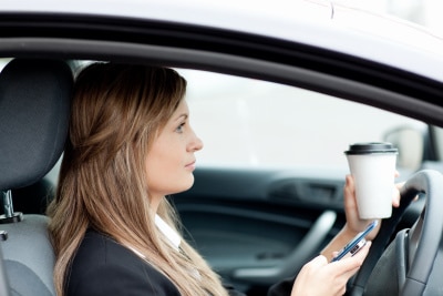 woman stopping her car while sipping coffee, checking her phone