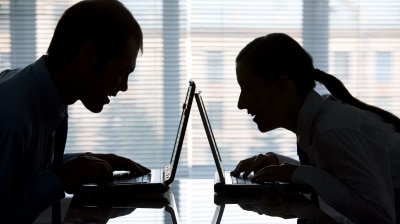 a silhouette of a man and woman on their laptops facing each other