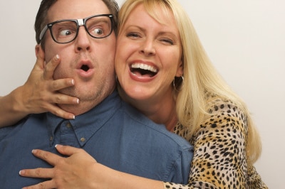 a grinning blonde woman embracing closely a man with an eyeglasses