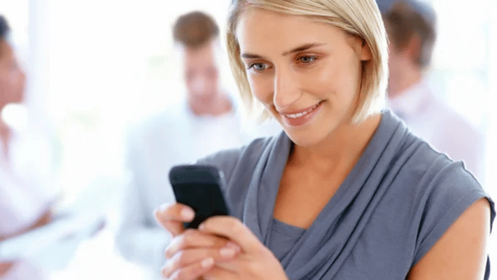 Closeup of beautiful woman reading text message with team in background