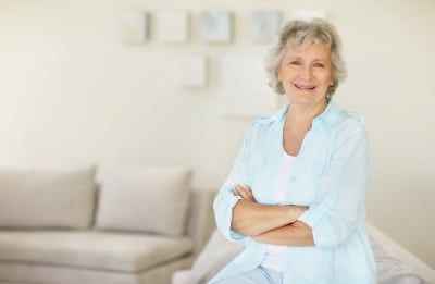 Portrait of a happy senior woman with hands folded relaxing on sofa at home