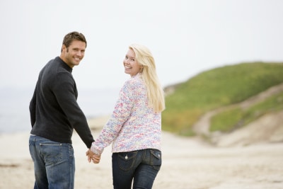 young couple holding hands while walking on the beach