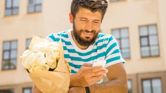 bearded guy holding flowers while texting and hoping to get ex back