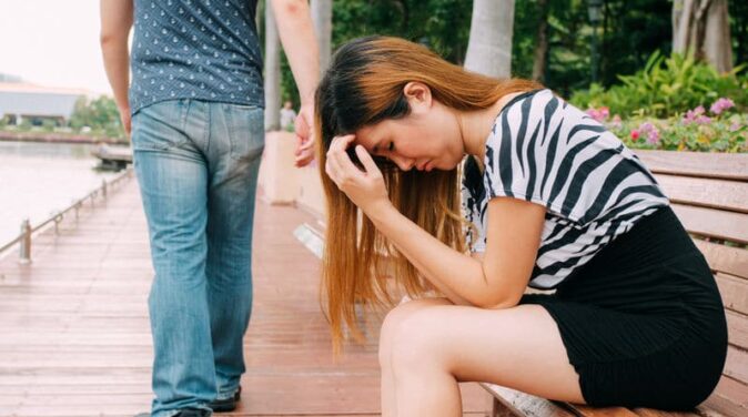 boyfriend breaking up with his girlfriend who is sitting on a bench