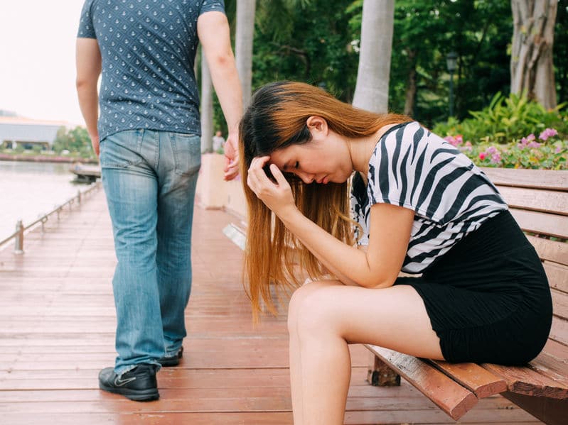 boyfriend breaking up with his girlfriend who is sitting on a bench