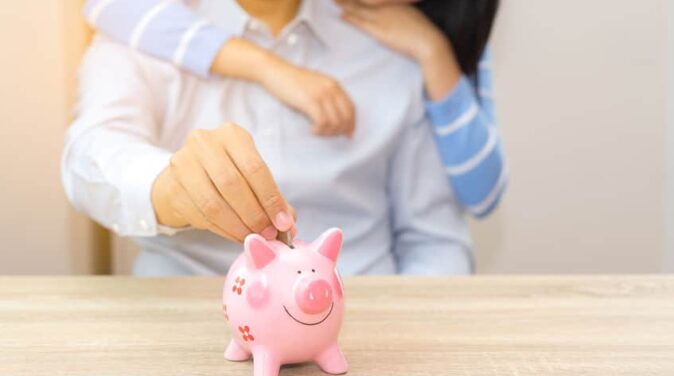 Smile couple putting a coin into a pink piggy bank on wooden desk - save money for the future