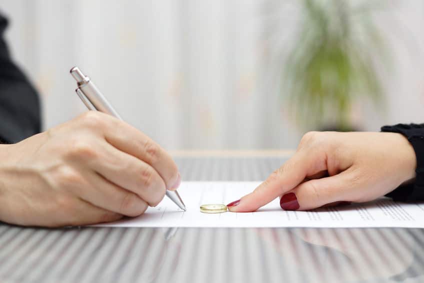 husband signing divorce agreement and woman push away weeding ring