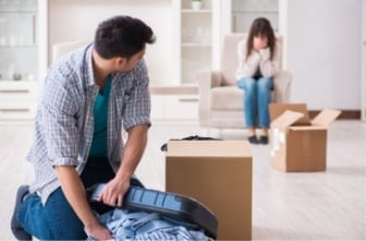 man packing his things while his wife cries on the couch