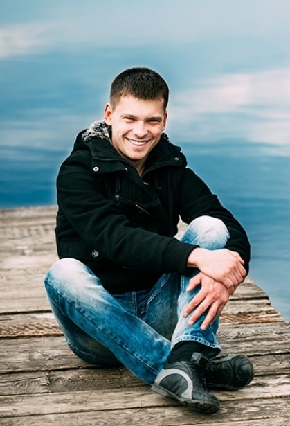 a happy man wearing black jacket sitting on a deck