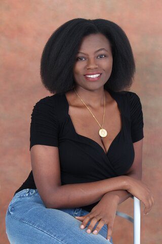 a woman with black curly hair wearing a gold necklace smiling