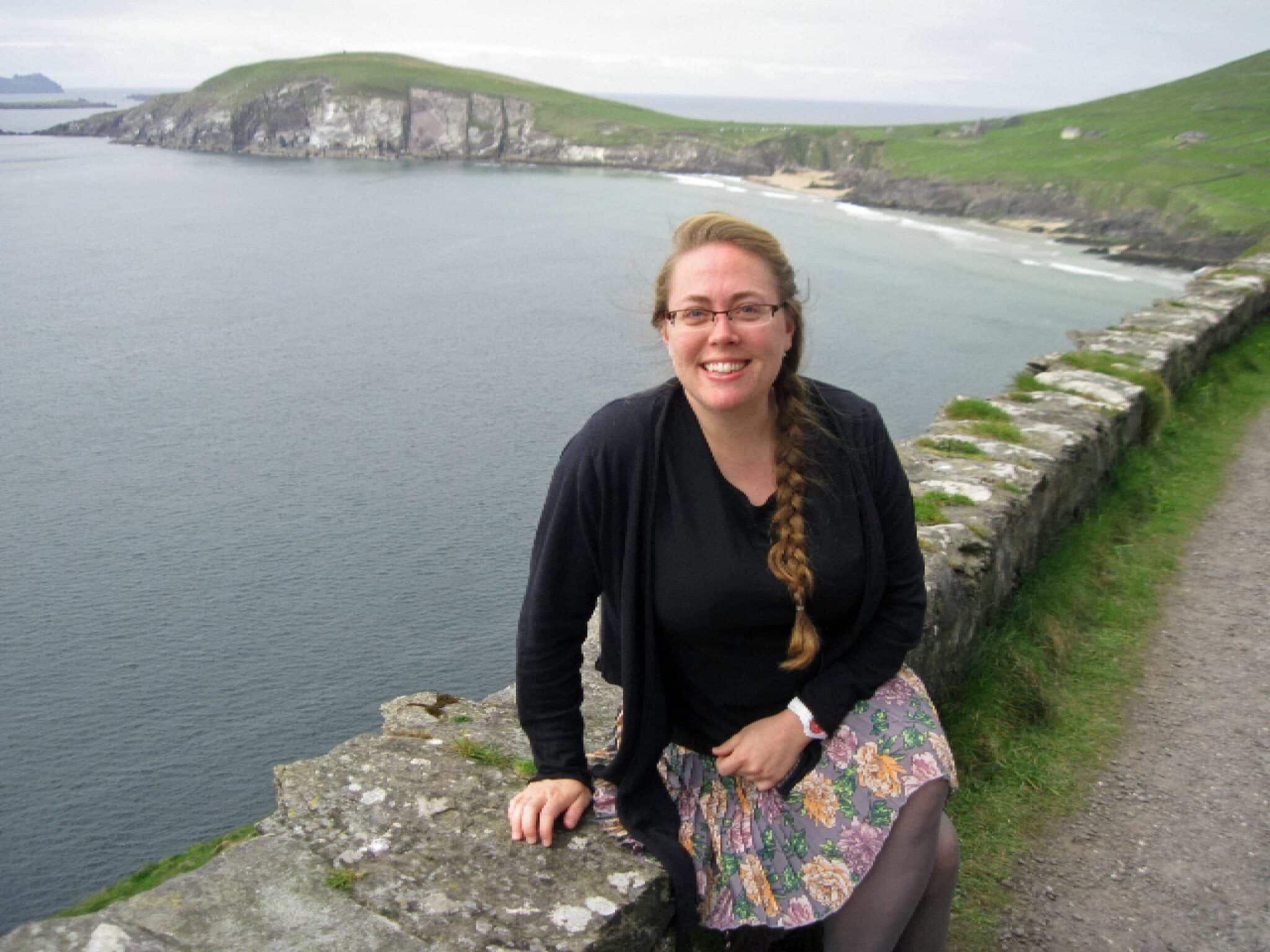 a woman in black and floral skirt sitting on a stone fence