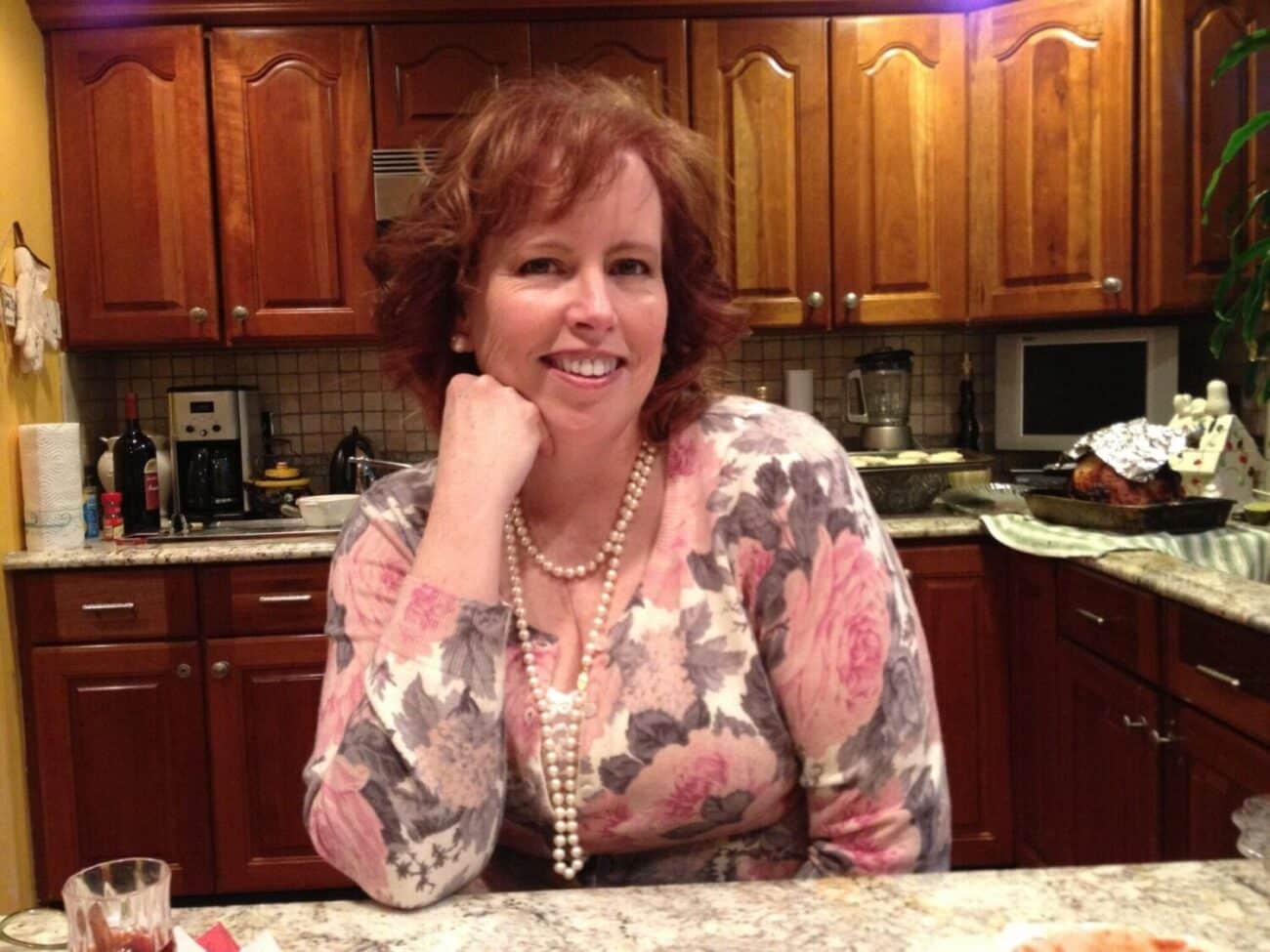 woman in the kitchen wearing a floral top smiling